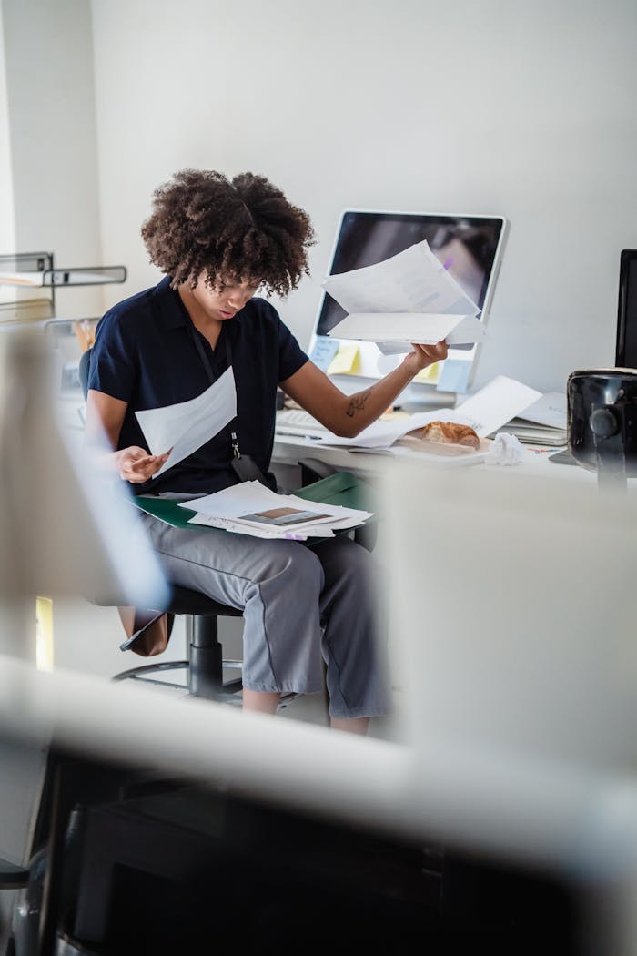 Busy office worker sorting through paperwork at her desk, concentrating on tasks.
