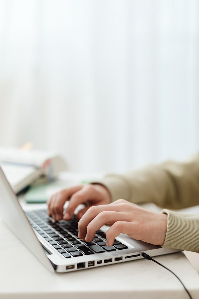Close-up of hands typing on a laptop, illustrating remote work in a modern, indoor setting.